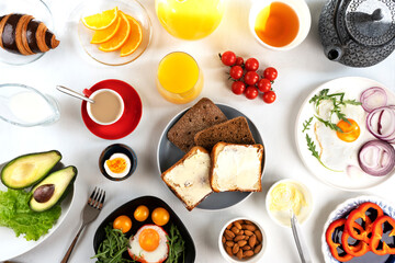 Delicious family breakfast table with coffee, tea, orange juice, croissants, toast, butter, fried and boiled eggs, avocado, cherry tomatoes, almond and salad. Top view.