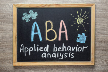 Small blackboard with text ABA Applied behavior analysis and drawings on wooden table, top view - obrazy, fototapety, plakaty