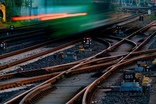 Railway tracks at main station of Hagen Westphalia Germany with switches and blurred leaving train in motion. Railway infrastructure and technology background at morning twilight. 