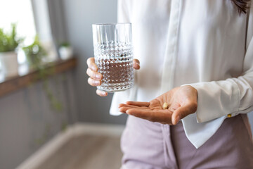Close up woman holding pill in hand with water. Female going to take tablet from headache,...
