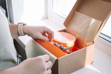 Cropped image of woman hands packing shipment with silicone kids dishes in box for delivery,...