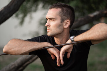 Portrait of a young handsome man with unshaven bristles in a black T-shirt leaning on a wire