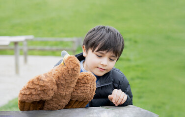 Happy young boy sitting on bench playing with bird toy in the park on sunny day morning, Kid playing in spring fields, Positive Child with smiling face relaxing or having fun on outdoor activity.