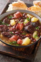 Sopa da Pedra traditional recipe combines red kidney beans, potatoes, cured meat and sausages closeup in the plate on the table. Vertical