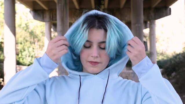 Smiling Teenage girl wearing blue oversize hoodie. Blue haired teen girl staying outdoors against bridge pillars. Mockup, head shot. Hipster and adolescence concept