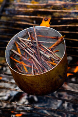 Survival in wild nature. Campfire background. Pan with cherry tea sticks over fire. Cooking tea...