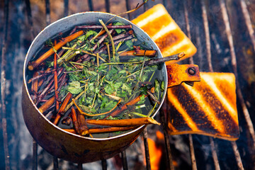 Survival in wild nature. Campfire background. Pan with cherry tea sticks over fire. Cooking tea...