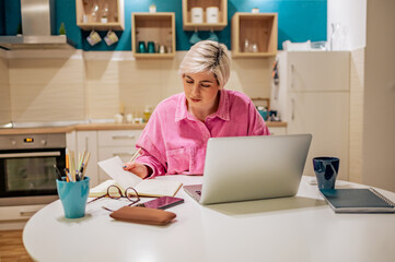 Woman with short hair working on a laptop at home and writing notes