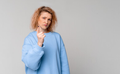 Serious middle age woman with curly blonde hair shaking her finger, scolding or telling off...