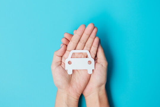 Hand Holding Paper Car Cutout On Blue Background. Vehicle Insurance, Warranty, Automobile Rental, Transportation, Maintenance And Repair Concept