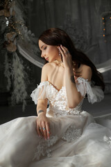 Fototapeta premium Woman Bride in a white dress is sitting on the floor by the window. A romantic image of a woman with a tattoo on her arm. Wedding