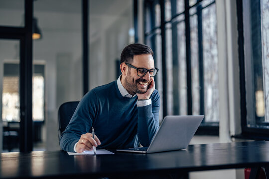 Smiling man with glasses on, using a laptop, at his office.