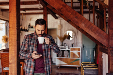 Man enjoying the morning, reading online news over the phone, drinking coffee.