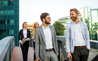 Group of cheerful young business people talking to each other while walking outdoors