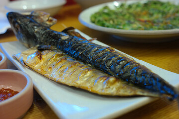 Grilled mackerel is served on a white plate.