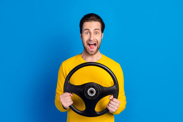 Portrait of attractive amazed cheerful brunet guy holding steering wheel having fun isolated over bright blue color background