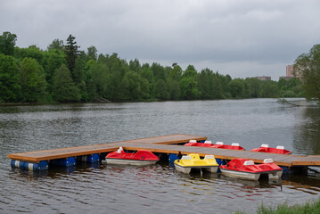 Fototapeta premium The park. A lake with catamarans, a bridge, multi-story buildings, trees.