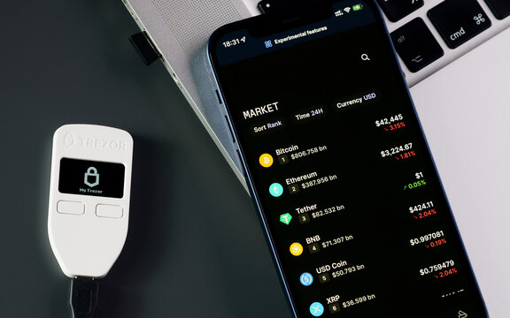 Amsterdam, Netherlands - April 8, 2022: Trezor hardware wallet for cryptocurrency and cryptocurrency market on iphone display.