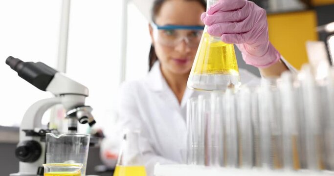 Scientist chemist shaking yellow liquid in flask and looking through microscope 4k movie