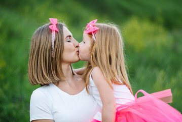 Young mother kissing a girl in the park. Family holiday. Portrait mom with child together on nature. Mum, little daughter walk in a field, outdoors. Happy Mothers Day. Close up.