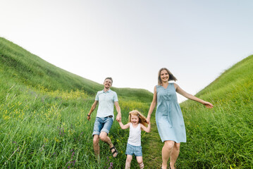 Mom, dad and daughter walk in the green grass. Happy young family spending time together, running outdoors. The concept of family holiday.
