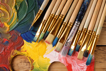Many paintbrushes and palette on wooden table, flat lay