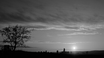 Colorful sky and distant city panorama at sunrise. Black and white photo.