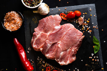 raw meat on a black board with chili, papper , garlic and rosemary
