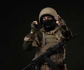 a Russian soldier in military clothes with a Kalashnikov assault rifle on a dark background takes...
