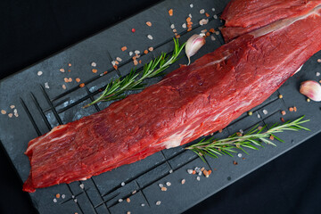 raw meat on a black board with salt, garlic and rosemary
