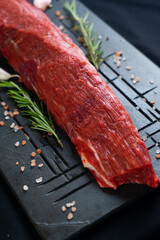 raw meat on a black board with salt, garlic and rosemary