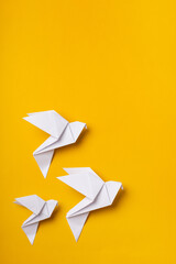 White origami doves as a symbol of faith, hope and peace on a yellow background