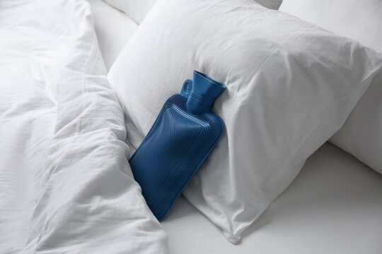 Rubber hot water bottle near soft pillow on bed