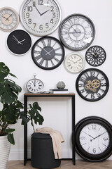 Console table, beautiful houseplant and collection of different clocks on white wall in room