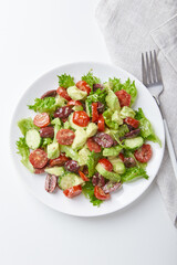 Salad with lettuce, cucumbers, tomatoes, olives and avocados in white plate on the table