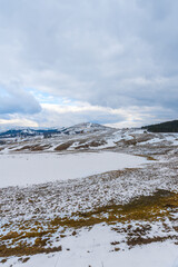 Snow fell on the dry grass. on mountain with cloudy sky close