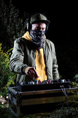 DJ vertical chico pincha musica con una mesa de mezclas en una fiesta en bosque vestido con una...
