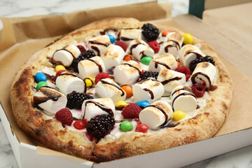 Tasty sweet pizza with berries, marshmallows and candies in cardboard box on table, closeup