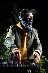 DJ vertical chico pincha musica con una mesa de mezclas en una fiesta en bosque vestido con una...