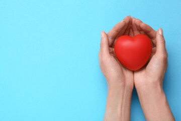 Woman holding red decorative heart on light blue background, top view and space for text. Cardiology concept