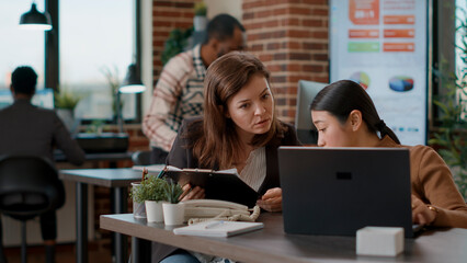 Business women brainstorming ideas to plan growth analysis, using statistics on papers and laptop in disability friendly office. People doing teamwork on financial charts development.