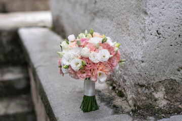 Beautiful bridal bouquet of white flowers and greenery, decorated with long silk ribbon lies on white background. Copy space
