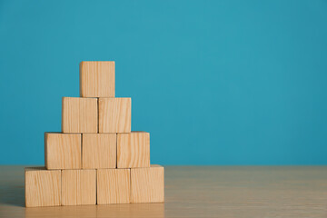Pyramid of blank cubes on wooden table against light blue background. Space for text