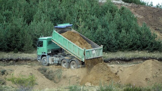 Construction truck dumping, unloading gravel on road construction site, preparing ground for new housing estate