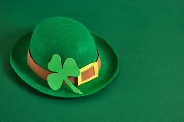green felt hat in the style of a leprechaun and a clover leaf from foamiran on a green background