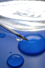 Syringe needle with a drop of a transparent substance and a glass jar close-up