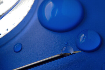 Syringe needle with a drop of a transparent substance and a glass jar close-up