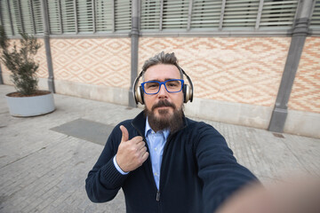 Mid adult man taking selfie and showing thumbs up while listening to music