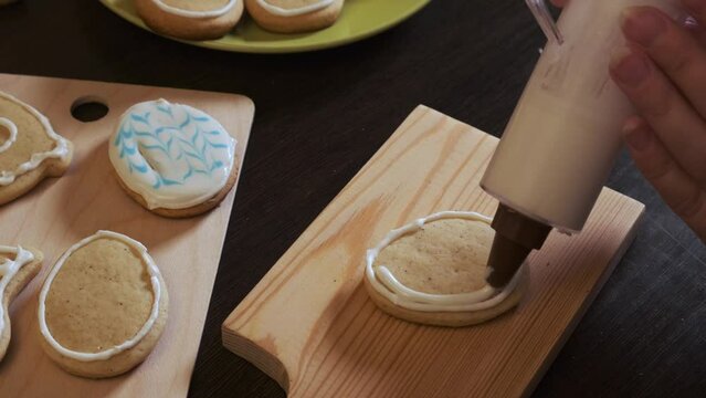 Close-up of women's hands apply icing to cookies using a cooking syringe. cookies in the form of an Easter egg.