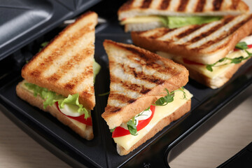 Modern grill maker with sandwiches on table, closeup view